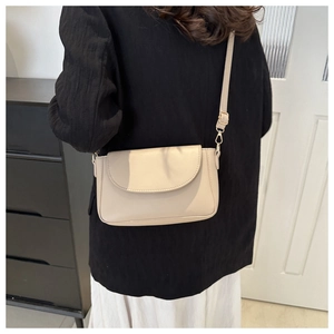 Close-up of beige crossbody bag with gold hardware and adjustable strap on a model