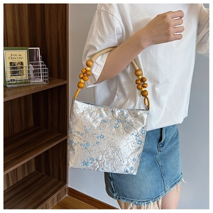 Detail of silk bucket bag showing wood bead handle and blue floral pattern on silver fabric