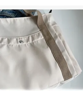 Detailed macro shot of ivory canvas tote fabric with glossy finish and brown woven strap