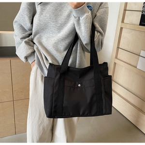Detail of black nylon tote bag featuring front metal snap pocket and sturdy woven handles