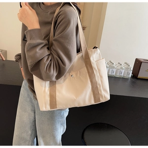 Detail of cream nylon tote bag featuring durable brown straps and metal buckle pockets