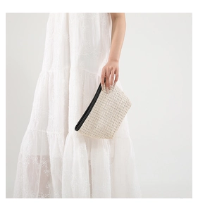 Dettaglio della pochette in paglia beige con zip nera a contrasto e trama intrecciata