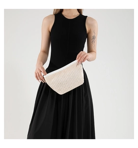 Dettaglio di una pochette in paglia intrecciata beige con finiture in PU tenuta da modella