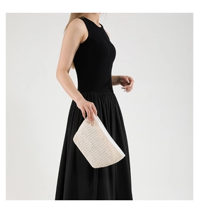 Dettaglio della pochette in paglia intrecciata con cerniera bianca su sfondo neutro