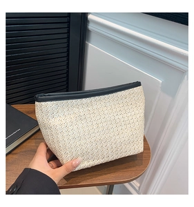 Dettaglio di pochette in paglia intrecciata crema con elegante bordo in ecopelle nera