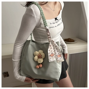 Detail of light green tote bag with floral pendant and scarf-wrapped woven strap