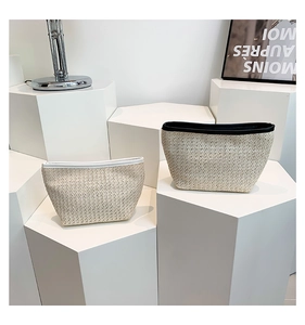 Dettaglio di pochette in paglia intrecciata con bordo bianco e nero su piedistalli moderni