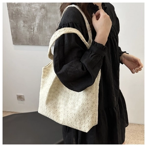 Detail of cream lace embroidery on tote bag styled with a black pleated dress
