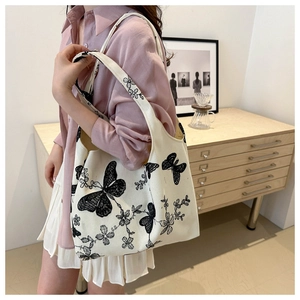 Detail of off-white canvas tote bag featuring black butterfly and floral embroidery art