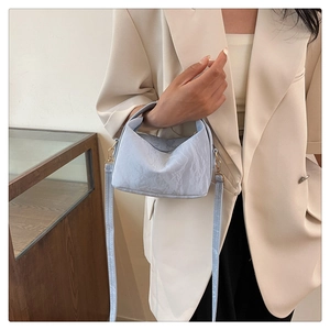 Detail of light blue pleated handbag with metallic hardware and slim shoulder strap