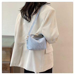 Detail of light blue pleated PU shoulder bag with gold clasp worn by model in suit