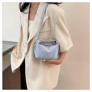 Detail of light blue pleated PU cloud bag with gold buckle on white blazer model