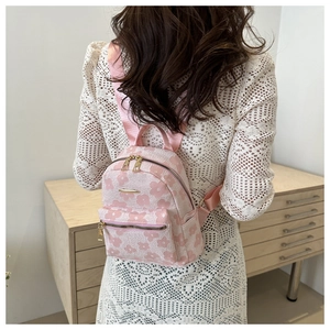 Pink embroidered backpack with white flowers worn by model in a cozy indoor setting