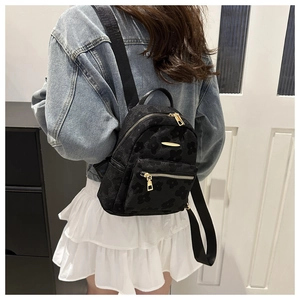 Close-up of black mini backpack with floral embossing and gold hardware on model