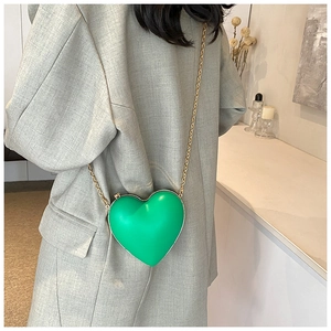 Gros plan d'un sac à main cœur vert vif avec chaîne dorée porté par un modèle