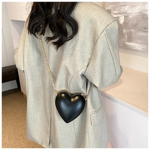 Detailed view of a black heart-shaped crossbody bag with gold chain worn by a model