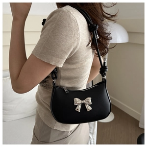 Close-up of black crossbody bag featuring a silver metal bow and unique knotted shoulder strap