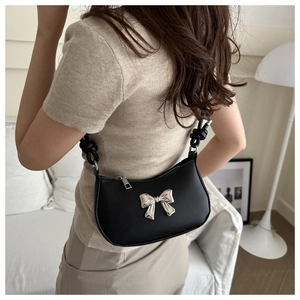 Detail of black crescent shoulder bag with silver bow accent and knot strap on model