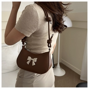 Detail view of brown shoulder bag with silver bow charm and knotted strap design