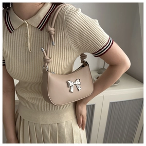 Close-up of beige moon-shaped underarm bag with silver bow charm and knotted shoulder strap