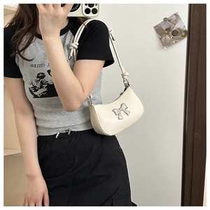 Detail of white half-moon bag featuring a metallic silver bow on smooth faux leather