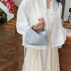 Silver metallic pleated handbag with adjustable strap shown in a stylish indoor setting