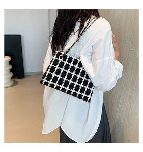 Detail of black and white plaid tweed shoulder bag with gold chain strap on a person