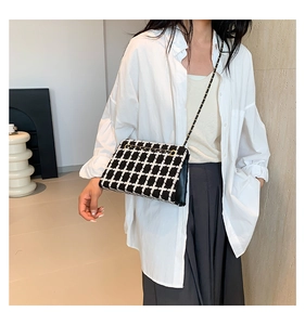 Detail of checkered tweed crossbody bag with gold chain strap on a white shirt