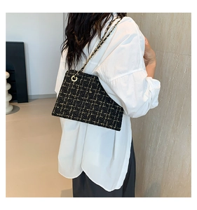 Detail of black tweed crossbody bag with gold chain strap on white shirt