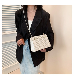 Detail of tweed crossbody bag with gold chain strap on a model wearing black blazer