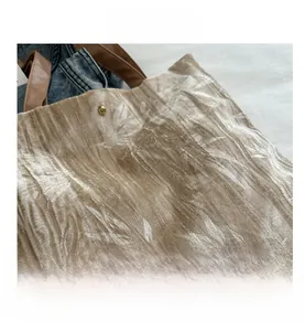 Close-up of pleated champagne velvet fabric and gold magnetic clasp on tote bag