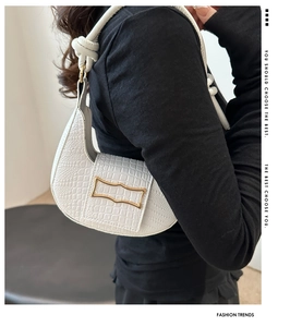 Detail of white crocodile embossed half-moon bag with gold buckle and knot strap detail
