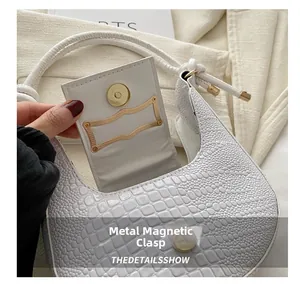Detail of light gold magnetic clasp on white crocodile pattern crescent underarm bag