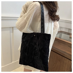 Detail of black pleated tote bag with golden metal dot and leather shoulder strap on model