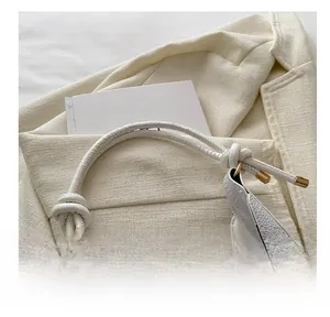 Macro detail of white crocodile-embossed leather handle with gold hardware on crescent bag