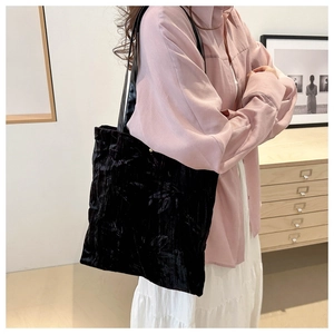 Detail of black velvet tote bag with floral embroidery worn by a model in a cozy interior