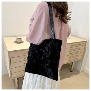 Detail of black pleated velvet tote bag showing fabric texture and leather shoulder strap