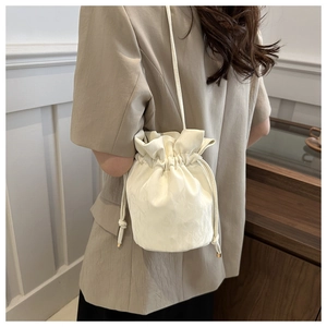 Detail of white drawstring bucket bag showing textured pleats and slim shoulder strap