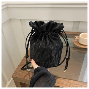 Detail of black drawstring bucket bag showing pleated glossy texture and gold metal tips