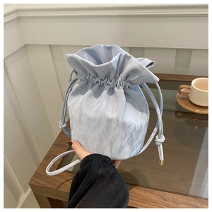 Light blue drawstring bucket bag with unique crinkled texture held against a minimalist backdrop