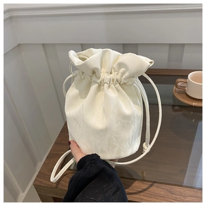 Close-up of cream drawstring bucket bag with pleated texture and thin shoulder strap