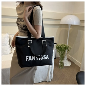 Detail view of black canvas tote bag with FANYISSA lettering and white leather trim accents
