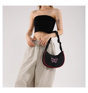 Détail du sac croissant noir avec broderie papillon rose et bandoulière à volants