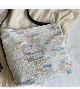 Gros plan sur le gaufrage géométrique et les broderies colorées du sac en toile blanc