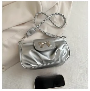 Sac argenté plissé avec nœud et bandoulière tressée montré avec un smartphone pour taille