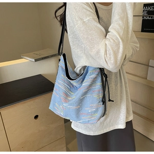 Détail du sac en toile brodé bleu clair avec motifs de vagues colorés et cordon noir