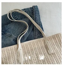 Detailed macro view of beige woven straw tote bag with smooth cream faux leather handles