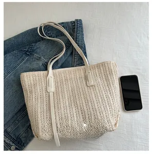 Detail of a beige woven tote bag with smooth leather straps next to a smartphone