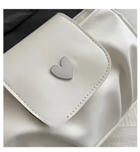 Close-up of white pleated leather bag featuring a silver heart-shaped metal buckle detail