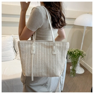 Detail of woven straw tote bag with cream leather straps in a bright minimalist setting